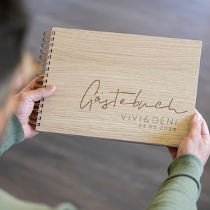 May include: A wooden guest book with a spiral binding. The cover is engraved with the text "G&auml;stebuch" and "VIVI & DENI 24.05.2024".