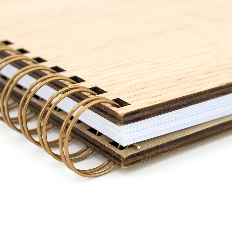 May include: A wooden spiral bound notebook with a gold metal binding. The notebook has a natural wood grain finish and a dark brown edge.