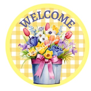 May include: A round welcome sign with a yellow and white checkered background. The sign features a blue bucket filled with a colorful bouquet of flowers, including tulips, daffodils, and irises. The word "WELCOME" is written in purple letters on the sign.