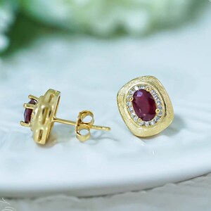 Peut inclure: Une paire de boucles d'oreilles en or avec une pierre ovale rouge entourée de petites pierres blanches. Les boucles d'oreilles ont une finition texturée et martelée.