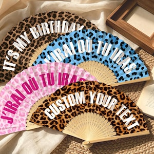 Könnte beinhalten: Vier Faltfächer mit Holzrippen und Stoffbespannung mit Tiermustern. Die Fächer zeigen die Texte IT'S MY BIRTHDAY, J'IRAI OÙ TU IRAS in Blau, J'IRAI OÙ TU IRAS in Pink und CUSTOM YOUR TEXT in weißer Schrift auf den Stoffen.