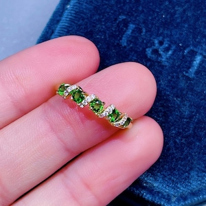 May include: A gold band ring with a row of green gemstones and smaller white gemstones set in the band.