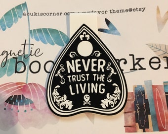 May include: Black and white ouija board-shaped bookmark with the text "Never Trust the Living" and a skull and crossbones symbol.