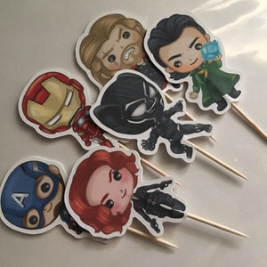 May include: Set of six superhero character cake toppers. The toppers feature Iron Man, Captain America, Thor, Black Widow, Black Panther, and Loki. Each topper is printed on white cardstock and attached to a wooden stick.