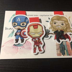 Op de afbeelding: Drie magnetische bladwijzers met superhelden-thema: Captain America, Iron Man en Thor. De bladwijzers zijn ge&iuml;llustreerd in een cartoon-stijl met een kleurrijke achtergrond.