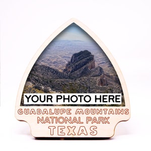 May include: Wooden cutout of a mountain range with a photo insert. The cutout is shaped like a mountain peak and has the text "YOUR PHOTO HERE" at the top, "GUADALUPE MOUNTAINS NATIONAL PARK" in the middle, and "TEXAS" at the bottom.