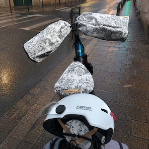 Peut inclure: Un vélo équipé de moufles de guidon et d'une housse de selle assortie au motif toile de jouy noir et blanc. Un casque blanc Himo Guardian avec visière transparente repose sur la selle, doté d'un petit insert en tissu assorti à l'arrière.