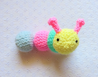 May include: A crocheted caterpillar toy with a light blue, pink, and yellow body. The caterpillar has two pink antennae and black eyes.