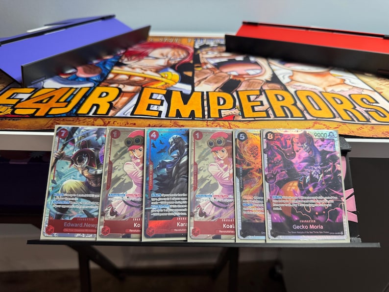 May include: Five trading cards featuring characters from the anime One Piece. The cards are arranged in a row from left to right. The characters are Edward Newgate, Koala, Karoo, Koala, and Gecko Moria. The cards are all in a holographic style with a black background.