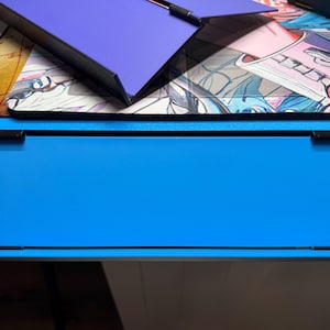 May include: A blue desk organiser with a black frame and a black top. The organiser has a shelf on the bottom and a flat surface on the top.