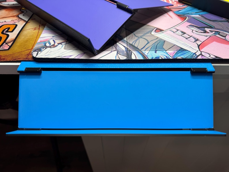 May include: A blue desk organiser with a black frame and a black top. The organiser has a shelf on the bottom and a flat surface on the top.