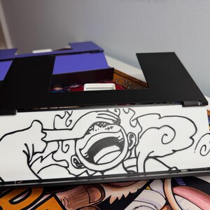 May include: A black frame with a white background and a black and white drawing of a cartoon character with a large smile and a cloud behind them. The character is covering their eyes with their hand.