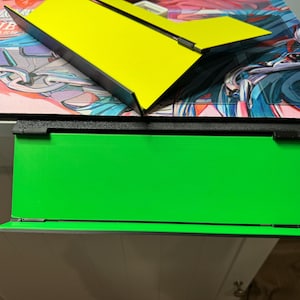 May include: A black frame with a green background. The frame is attached to a white surface.