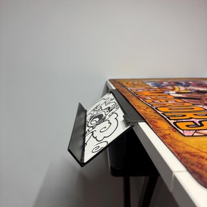 May include: A black metal desk organizer with a white and black cartoon design. The organizer is attached to the edge of a white desk with a black leg.
