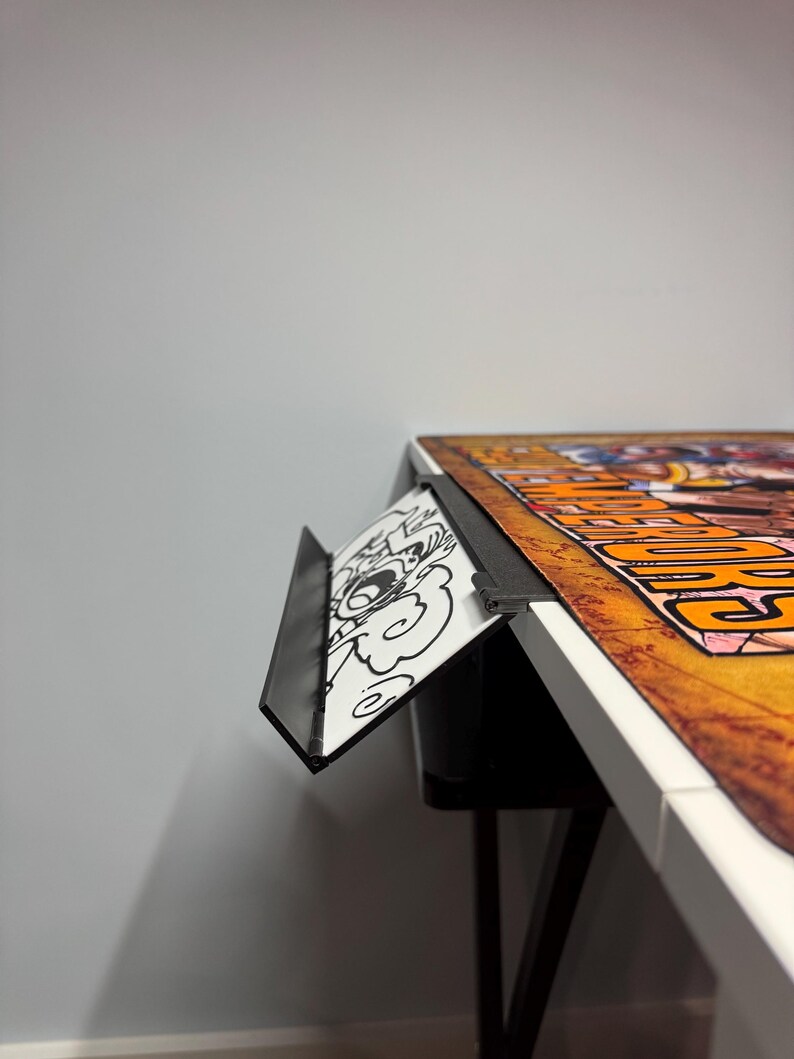 May include: A black metal desk organizer with a white and black cartoon design. The organizer is attached to the edge of a white desk with a black leg.