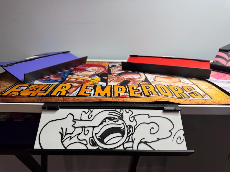 May include: A black and white illustration of a cartoon character with a large smile and a cloud behind them. The illustration is on a white background and is framed in a black frame. The frame is attached to a white desk with a black and orange anime-themed mousepad underneath.