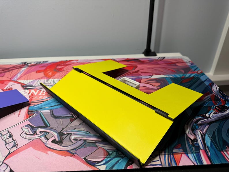 May include: A yellow cardboard box with a black border and a rectangular opening. The box is folded into a triangular shape.