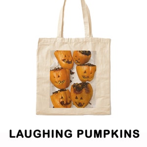 May include: A tote bag with a design of six orange bell peppers carved with jack-o'-lantern faces. The peppers are filled with a brown mixture and are arranged on a white surface. The text "LAUGHING PUMPKINS" is printed below the image.
