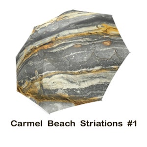 May include: A gray and yellow umbrella with a pattern of striations resembling rock formations. The umbrella is labeled "Carmel Beach Striations #1".