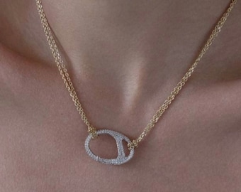 May include: A gold chain necklace with a diamond-encrusted oval pendant. The pendant has a cutout design in the center.