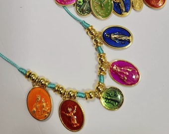 Puede incluir: Dos pulseras de cuerda turquesa con dijes de oro que representan figuras religiosas. Los dijes son de forma ovalada y tienen acentos de esmalte de colores. Las pulseras están atadas con un nudo y tienen un borla.