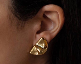 May include: Gold-toned geometric earrings with a folded design. The earrings are a modern and minimalist style.