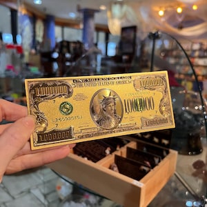 May include: A gold-colored paper bill with the text "ONE MILLION DOLLARS THE UNITED STATES OF AMERICA" and the number "1,000,000" printed on it. The bill features a depiction of the Statue of Liberty.
