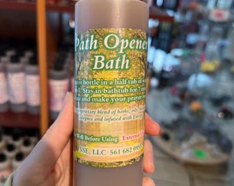 May include: A brown glass bottle with a black cap labeled "Path Opener Bath". The label has green foliage and text that reads "Pour bottle in a half tub of water. Stay in bathtub for 7 minutes and make your prayer request. Proprietary blend of herbs, oils, botanicals and infused with Energy. Well Before Using. External Use Only. SSE, LLC 561 682 0955"