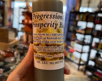 May include: A dark green glass bottle with a white label that reads "Progression Prosperity Bath". The label also includes instructions for use and contact information for SSE, LLC.