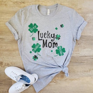 Puede incluir: Camiseta gris con el texto "Lucky Mom" y cuatro tr&eacute;boles con los nombres "Drew", "Landen", "Declan" dentro de cada tr&eacute;bol.