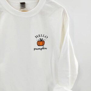 May include: White sweatshirt with a black and orange pumpkin graphic and the text "HELLO pumpkin" on the front.