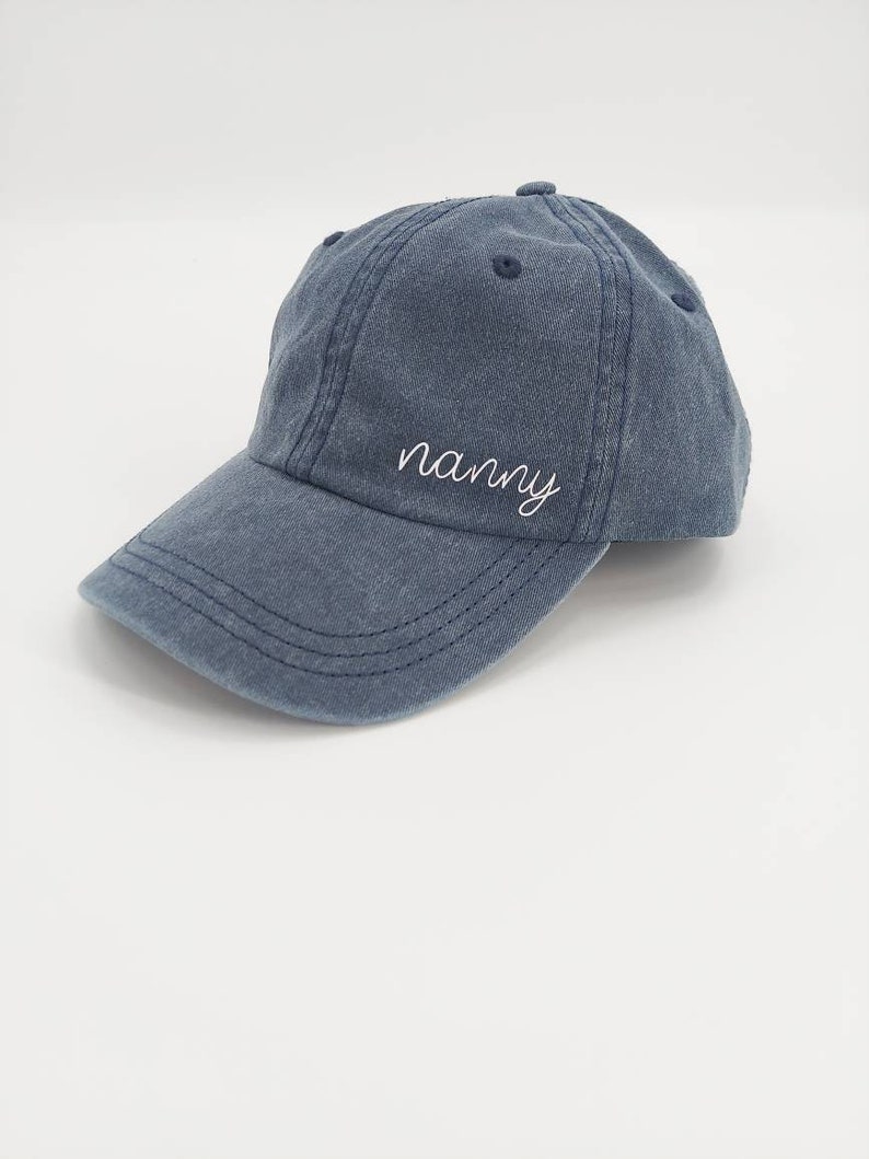 K&ouml;nnte beinhalten: Eine blaue Baseballkappe aus Denim mit dem Wort "nanny" in wei&szlig; auf der Vorderseite gestickt.