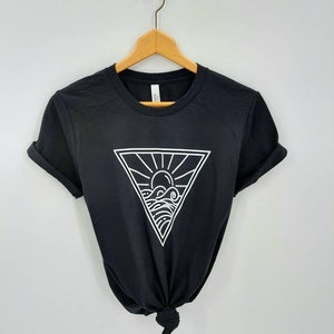 May include: Black t-shirt with a white graphic of a sun and waves inside a triangle.