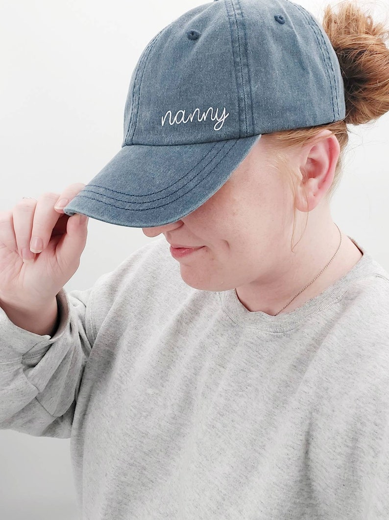 K&ouml;nnte beinhalten: Eine blaue Baseballkappe aus Denim mit wei&szlig;er Stickerei, auf der "nanny" steht.