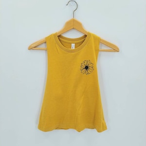 May include: A mustard yellow sleeveless tank top with a black daisy graphic on the front.