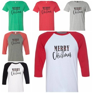 Op de afbeelding: Vijf verschillende T-shirts met de tekst "Merry Christmas" in zwarte letters. De shirts zijn in verschillende kleuren, waaronder groen, rood, grijs en wit. Twee van de shirts zijn in baseball-stijl met rode en zwarte mouwen.