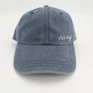 K&ouml;nnte beinhalten: Eine blaue Baseballkappe aus Denim mit dem Wort "nanny" in wei&szlig; auf der Vorderseite gestickt.
