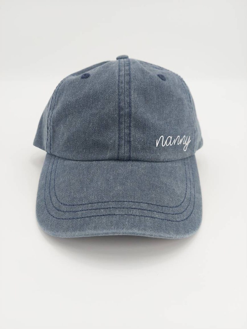 K&ouml;nnte beinhalten: Eine blaue Baseballkappe aus Denim mit dem Wort "nanny" in wei&szlig; auf der Vorderseite gestickt.