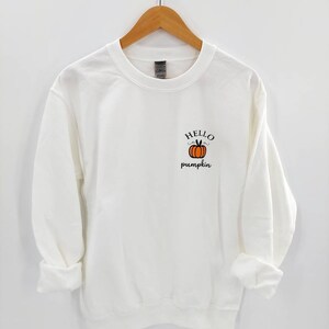 May include: White sweatshirt with a small orange pumpkin graphic and the text "HELLO pumpkin" on the front.