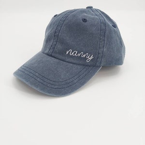 K&ouml;nnte beinhalten: Eine blaue Baseballkappe aus Denim mit dem Wort "nanny" in wei&szlig; auf der Vorderseite gestickt.