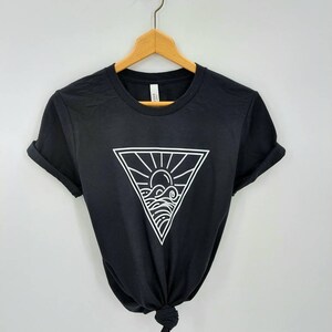 May include: Black t-shirt with a white graphic of a sun and waves inside a triangle.