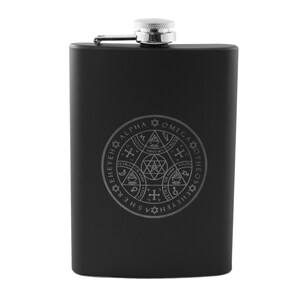 Op de afbeelding: Zwarte metalen fles met een zilveren dop en een zilveren gegraveerd ontwerp van een cirkel met de woorden "THEOS  OMEGA  ALPHA  SHE  REHE  YEHE  EHENE  ALPHA  OMEGA  THEOS" rond de buitenkant en een complex geometrisch ontwerp binnen de cirkel.