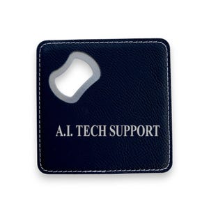 May include: A black leatherette bottle opener with a stitched border and a silver bottle opener. The text "A.I. TECH SUPPORT" is printed in white on the front.