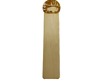 Puede incluir: Un marcapáginas de madera con un diseño circular de bisonte de pie en un bosque, cortado con láser. El marcapáginas es de color marrón claro y tiene un acabado liso y pulido.