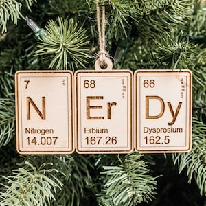 May include: Three wooden ornaments shaped like periodic table elements. The elements are nitrogen (N), erbium (Er), and dysprosium (Dy). Each ornament has the element's symbol, atomic number, atomic weight, and name.