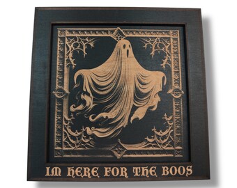 Op de afbeelding: Een houten kunstwerk in een frame met een spook met vloeiende gewaden, in tinten beige en zwart. Het ontwerp bevat gotische details. De zin "I'M HERE FOR THE BOOS" is onderaan gegraveerd.