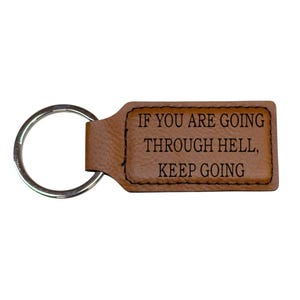 May include: Brown leather keychain with a silver key ring. The keychain has the text "IF YOU ARE GOING THROUGH HELL, KEEP GOING" engraved on it.