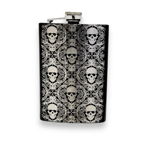 May include: Black stainless steel hip flask with a silver skull and floral pattern design.