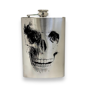 Könnte beinhalten: Eine silberne Trinkflasche mit einem eingeprägten Totenkopfdesign auf der Vorderseite. Der Totenkopf ist schwarz-weiß und hat ein detailliertes Design.