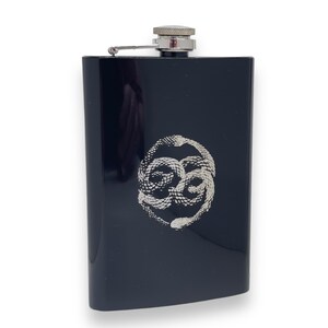 May include: Black stainless steel flask with a silver snake design. The flask has a screw-on cap with a hinged lid.